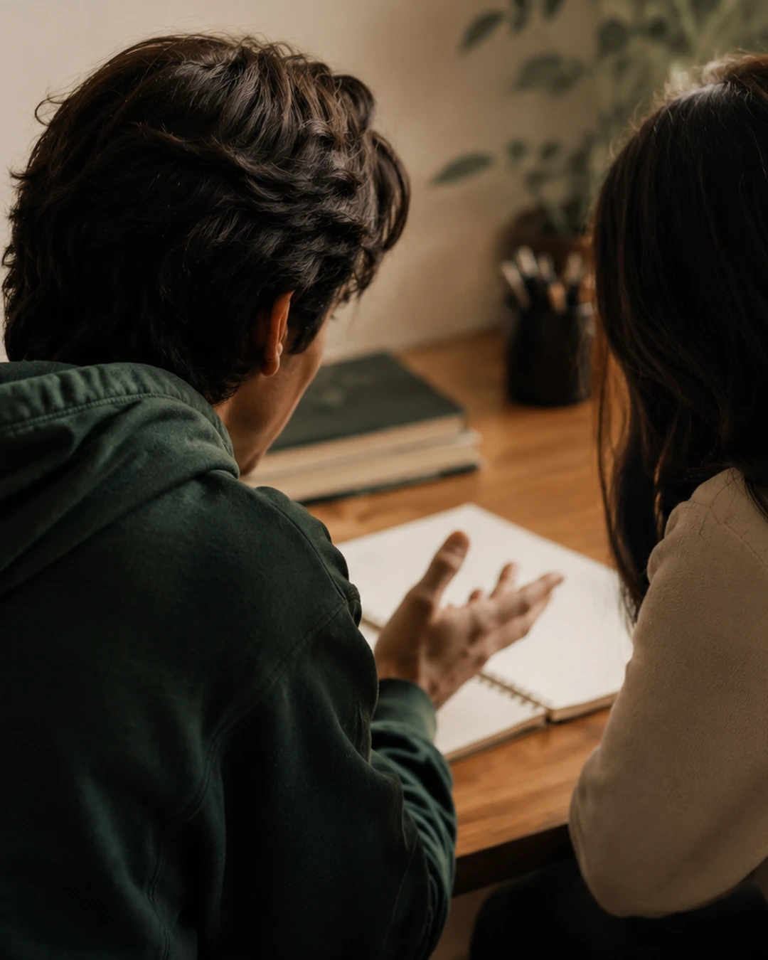 A mentor listening as a student talks through a notebook at a desk.